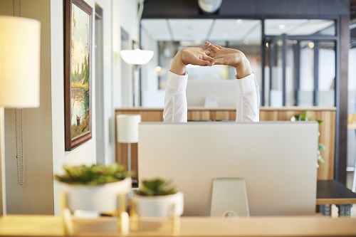 Person stretching behind a laptop while learning about Open Enrollment.