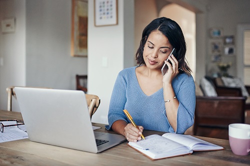 A woman talking on the phone while looking at her computer screen and taking notes.