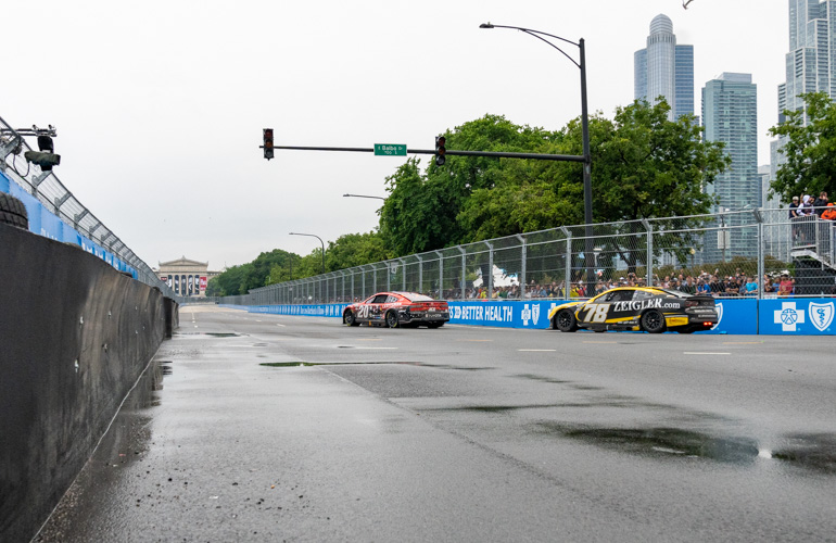 Water pools on the street and two racecars drive by.